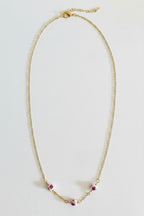 A delicate gold chain necklace with three small pink and white floral bead accents at the bottom center, displayed on a plain light gray background.