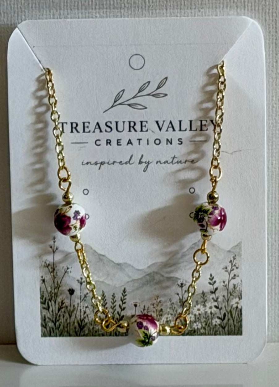 Treasure Valley Creations gold chain necklace with three pink and green floral bead charms, displayed on its white branded card.