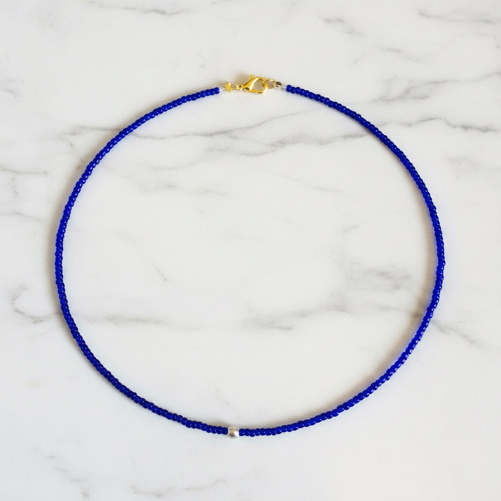 Blue beaded necklace with a gold clasp on a beige surface