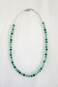 Green beaded necklace on a textured white surface