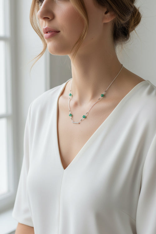 Woman wearing a delicate necklace with green gemstones against a neutral background