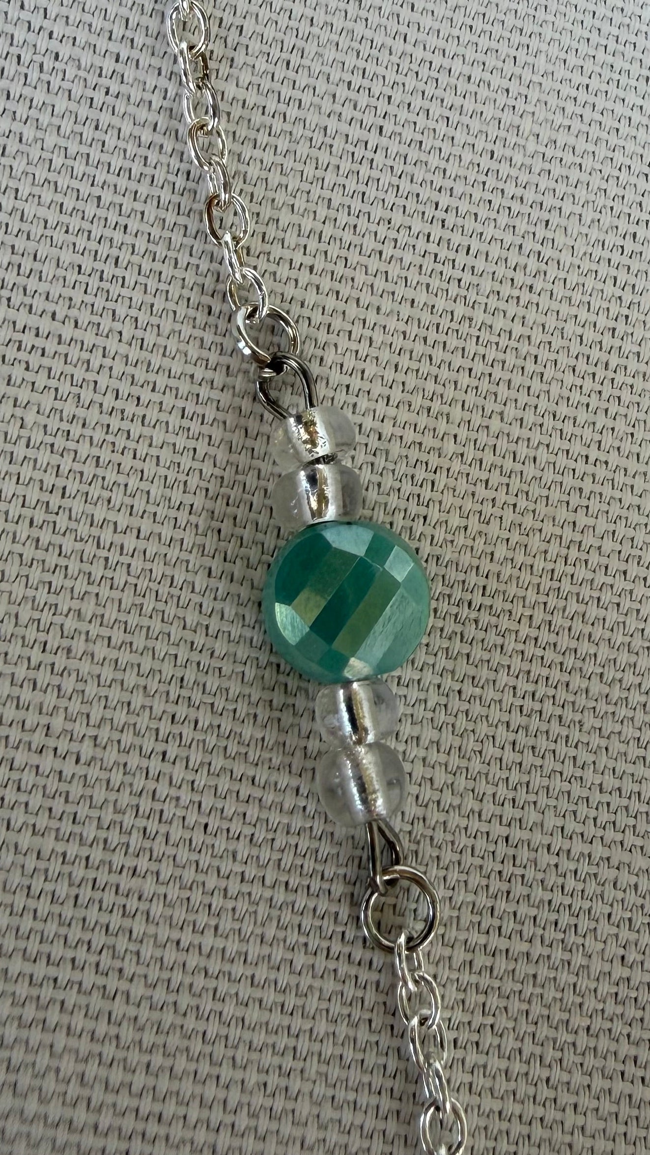 Close-up of a necklace with a green bead on a textured gray background