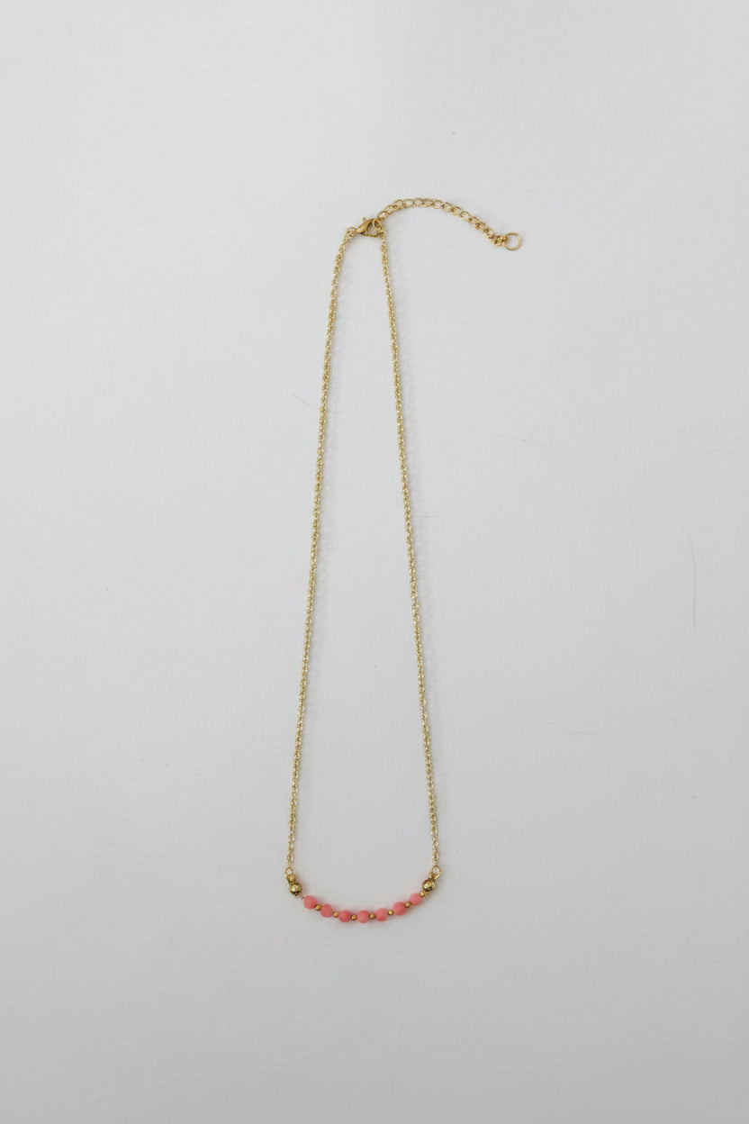 A delicate gold chain necklace featuring a short horizontal segment of small pink beads at the center, displayed against a plain light gray background.