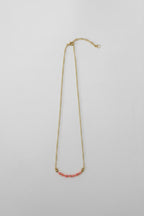A delicate gold chain necklace featuring a short horizontal segment of small pink beads at the center, displayed against a plain light gray background.