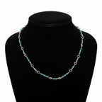 A silver link chain necklace with small turquoise-blue beads, displayed on a black velvet jewelry bust against a dark gray background.