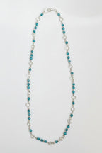 A beaded necklace featuring small teal-blue beads separated by silver-toned rings and a few silver-toned beads, with a silver clasp, shown on a plain light background.