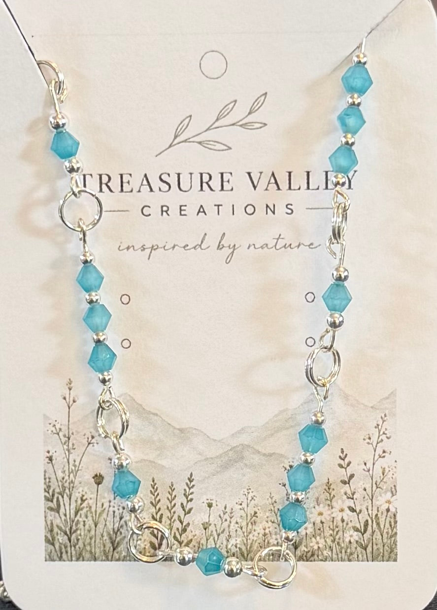 Handmade silver-tone necklace featuring faceted turquoise-blue crystal beads separated by polished silver links on an adjustable chain.