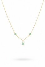 A delicate gold chain necklace featuring three small, light green faceted beads spaced along the chain, with a smaller green bead hanging from the center, set against a plain white background.