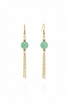 A pair of gold dangle earrings featuring a smooth, light green round bead and a delicate gold chain dangle, shown against a plain white background with a faint reflection below.