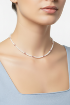 A close-up of a model wearing a delicate necklace made of small white and pink faceted beads, paired with a light blue top against a clean white background.