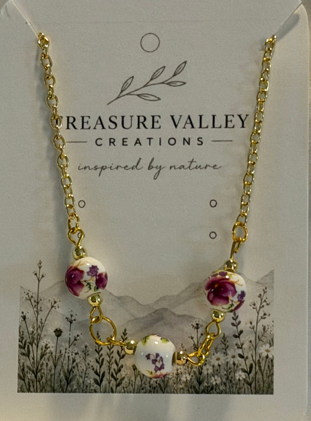 Treasure Valley Creations gold chain necklace with three floral ceramic beads, displayed on its branded card backing.