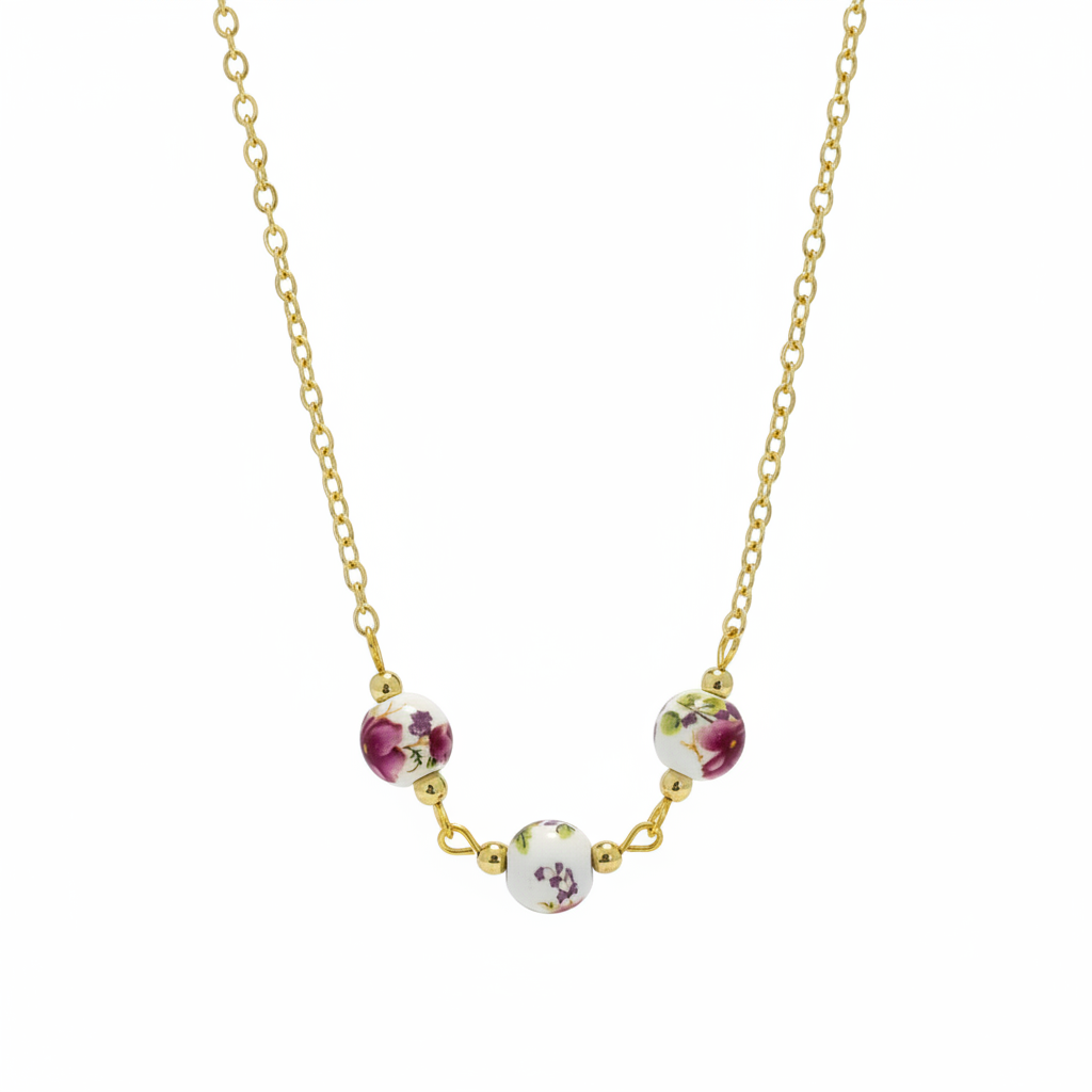 A gold chain necklace featuring three small round floral beads in white, pink, and green, arranged in an arc on a plain white background.
