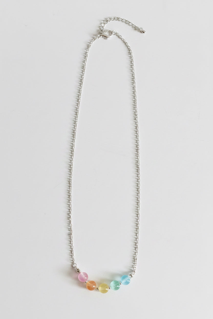 A silver chain necklace featuring five small, colorful round beads in pink, orange, yellow, green, and blue, arranged in a row at the center. The necklace is displayed flat against a light gray background.