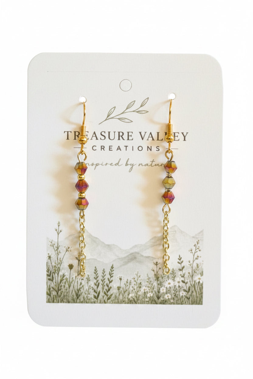 A pair of gold-tone beaded drop earrings with iridescent pink, yellow, and green beads, displayed on a white card from Treasure Valley Creations.