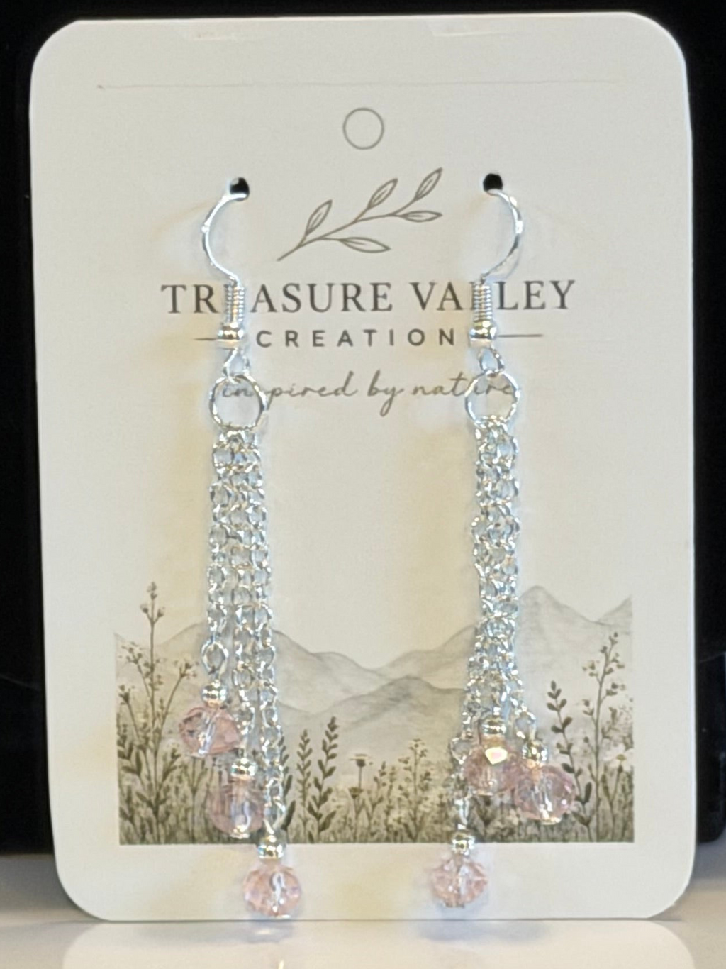 A pair of silver-tone dangle earrings with clear faceted beads and light pink crystal drops, displayed on a white Treasure Valley Creation branded card.