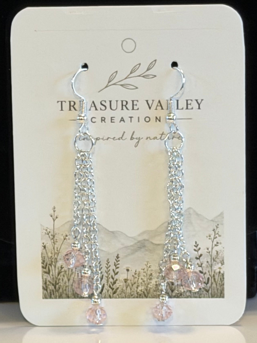 A pair of silver-tone dangle earrings with clear faceted beads and light pink crystal drops, displayed on a white Treasure Valley Creation branded card.