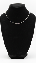 A delicate silver chain necklace with small blue displayed on a black velvet jewelry bust against a white background.