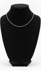 A delicate silver chain necklace with small blue displayed on a black velvet jewelry bust against a white background.