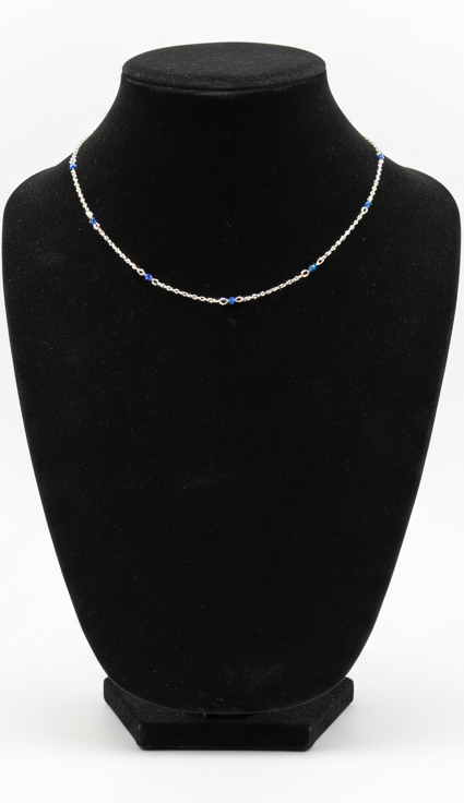 A delicate silver chain necklace with small blue displayed on a black velvet jewelry bust against a white background.