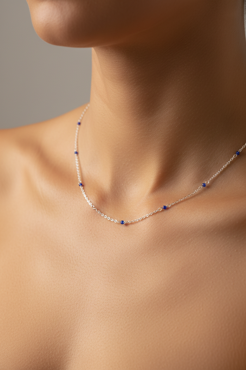 A delicate silver chain necklace with small blue bead accents, shown worn on a model's neck and upper chest against a soft gray background.