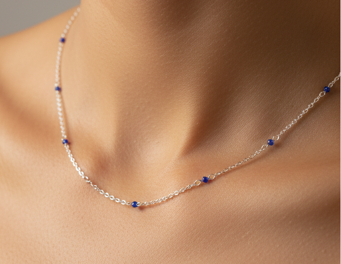 A delicate silver chain necklace with small, spaced blue gemstone accents, shown worn on a model's neck.