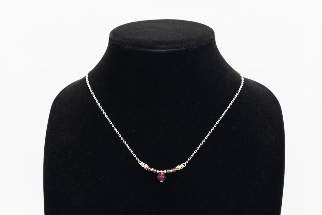 A delicate silver chain necklace with a small cluster of clear stones and a central faceted purple gemstone, displayed on a black velvet jewelry bust against a white background.