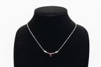 A delicate silver chain necklace with a small cluster of clear stones and a central faceted purple gemstone, displayed on a black velvet jewelry bust against a white background.