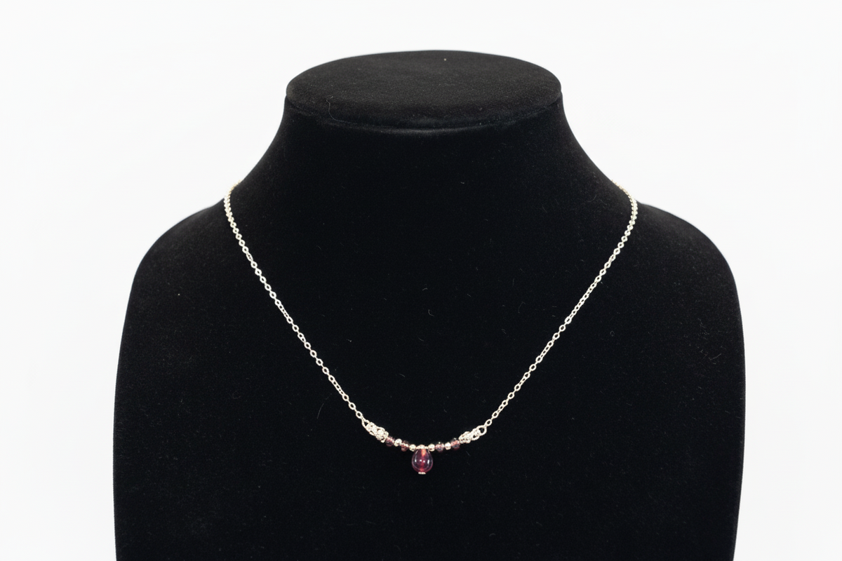 A delicate silver chain necklace with a small cluster of clear stones and a central faceted purple gemstone, displayed on a black velvet jewelry bust against a white background.
