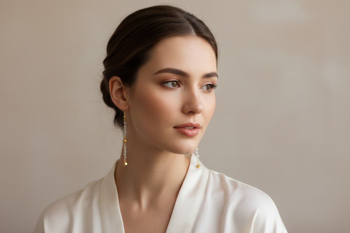 A pair of beaded drop earrings displayed on a cream-colored backing card. The earrings feature clear faceted beads with small gold spacer beads and gold-toned hooks.