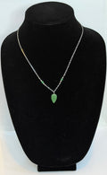 A delicate silver chain necklace with small green bead accents and a green teardrop pendant, displayed on a black velvet jewelry bust.