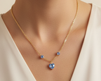 A gold chain necklace with a heart-shaped blue crystal pendant and two smaller blue crystal accents, shown worn on a model's neck.