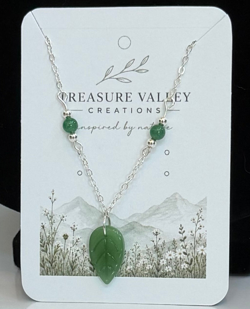 A small jewelry display card showing a green pendant necklace.
