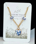 Treasure Valley Creations necklace featuring a gold chain with three blue and white floral bead-like charms and a matching heart-shaped pendant, displayed on a branded white card.