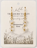A pair of gold drop earrings with clear semiprecious stone beads, displayed on a cream-colored backing card from Treasure Valley Creation.