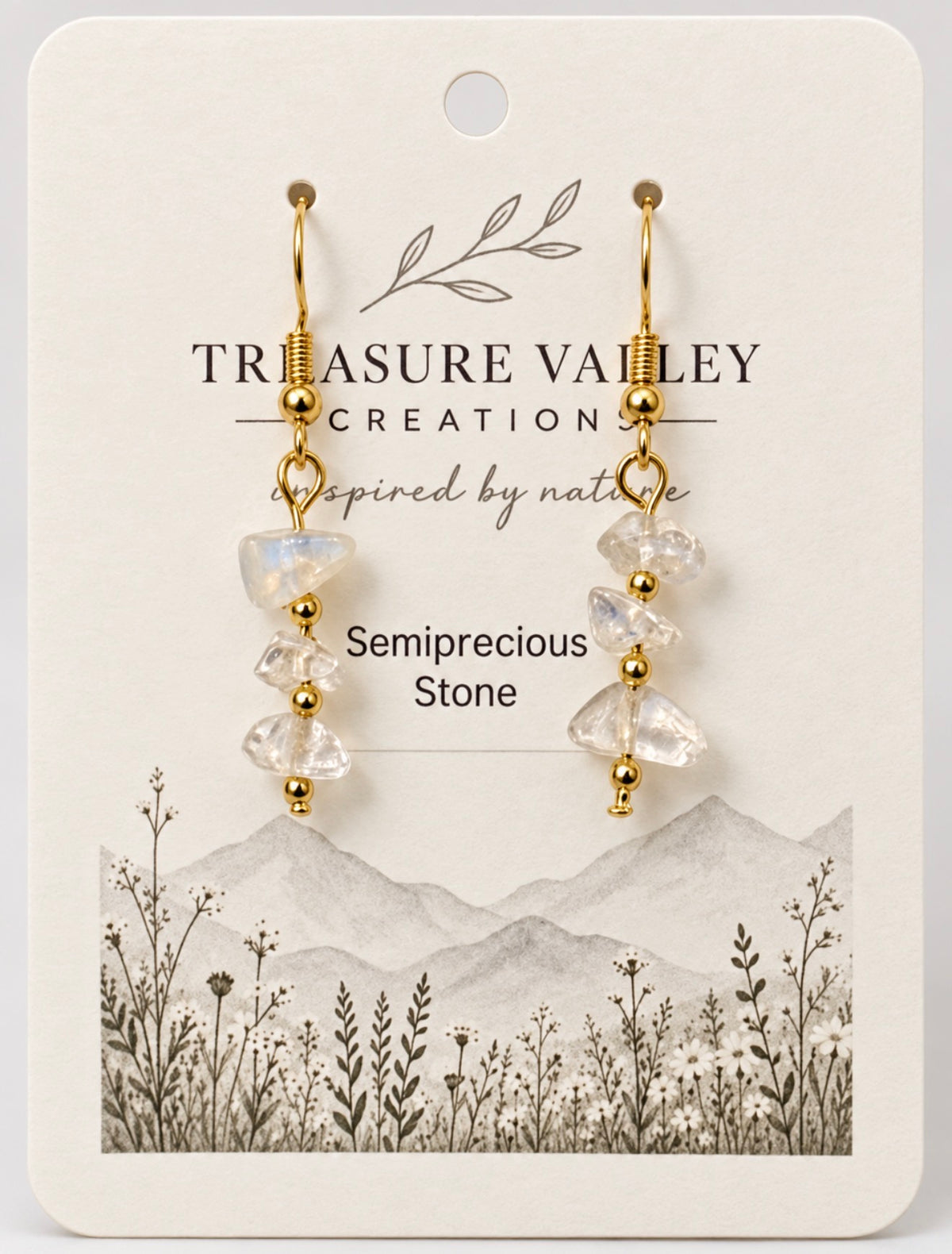 A pair of gold drop earrings with clear semiprecious stone beads, displayed on a cream-colored backing card from Treasure Valley Creation.