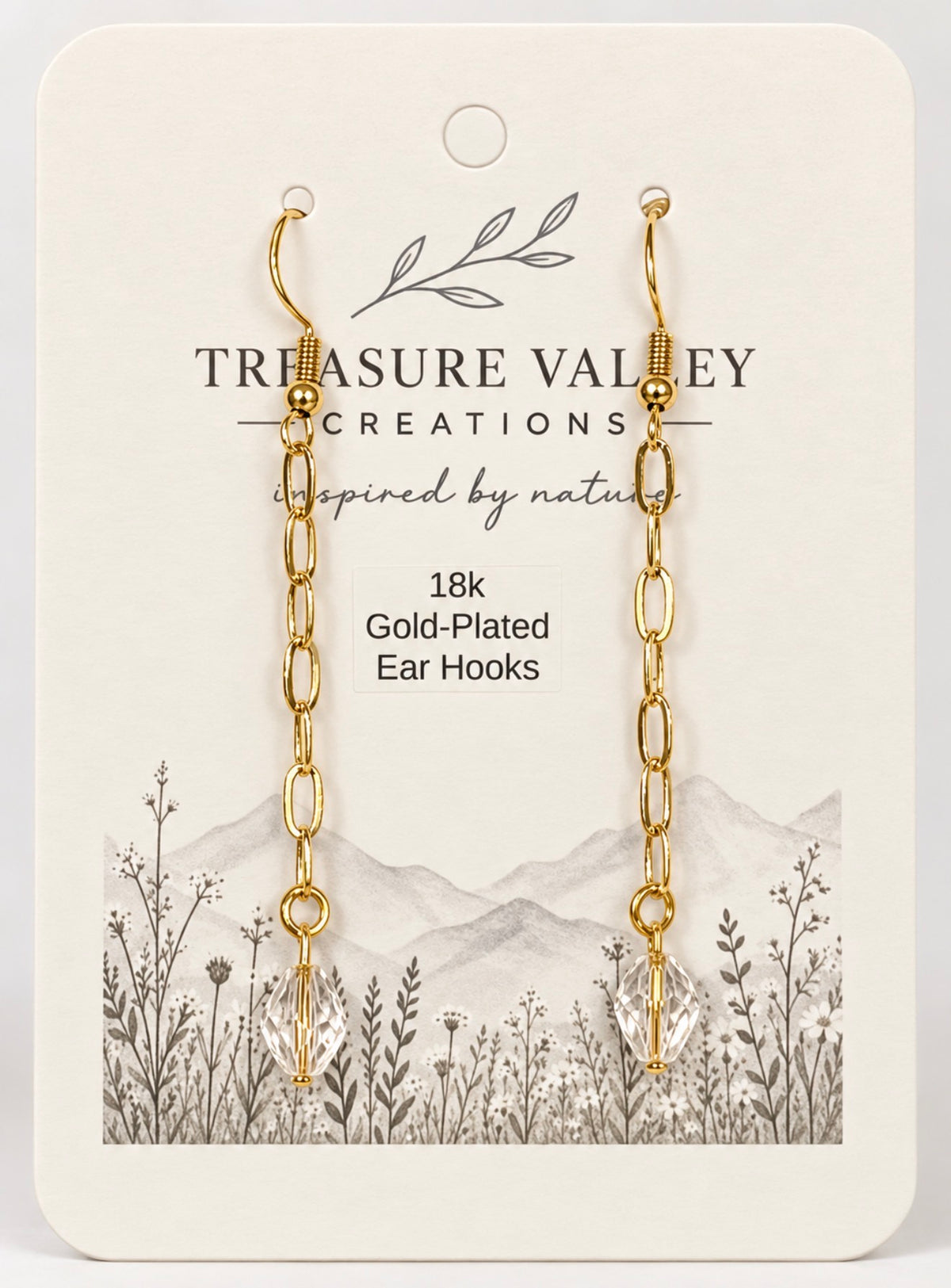 Treasure Valley Creations 18k gold-plated ear hooks on a cream-colored display card with a botanical and mountain illustration.