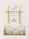 Treasure Valley Creations gold-plated ear hooks with clear faceted crystal drops, displayed on a cream-colored branded card with a mountain and wildflower illustration.