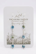 A pair of dangling earrings displayed on a white backing card. The earrings have silver-toned metal chains with faceted beads in shades of blue, teal, and olive green.