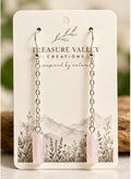 A pair of long dangle earrings with silver-toned chain links and pale pink cylindrical drops, displayed on a white backing card printed with the brand name Treasure Valley Creations.
