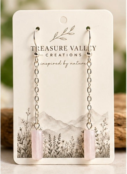 A pair of long dangle earrings with silver-toned chain links and pale pink cylindrical drops, displayed on a white backing card printed with the brand name Treasure Valley Creations.
