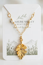 A gold leaf pendant necklace on a delicate chain, attached to a white display card