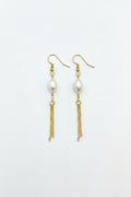 Pair of pearl earrings with gold chains on a gray surface