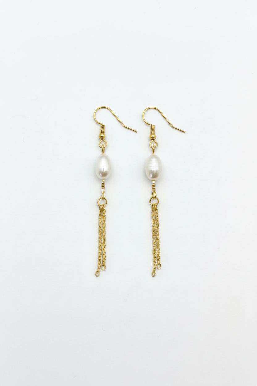 Pair of pearl earrings with gold chains on a gray surface