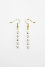 A pair of gold-tone dangle earrings with small white pearl beads, displayed on a clean white background.