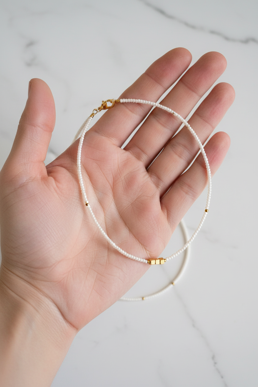 Hand holding a delicate necklace with gold clasps on a light background