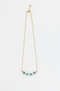 A delicate gold chain necklace featuring five small, faceted teal-green beads aligned in a curve at the center, displayed against a plain white background.
