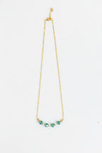 A delicate gold chain necklace featuring five small, faceted teal-green beads aligned in a curve at the center, displayed against a plain white background.
