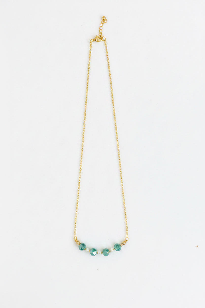 A delicate gold chain necklace featuring five small, faceted teal-green beads aligned in a curve at the center, displayed against a plain white background.