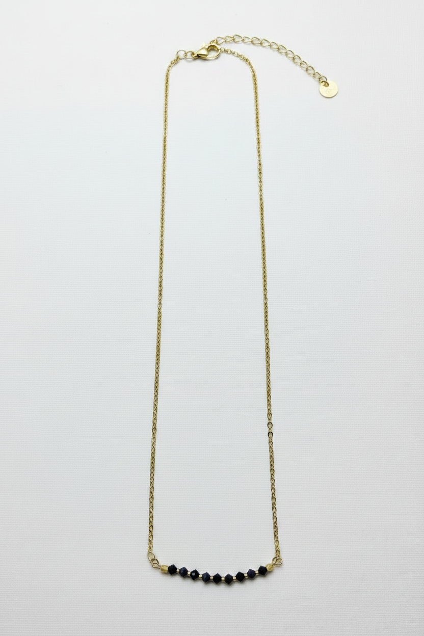 A delicate gold chain necklace with a short curved row of small black beads at the center, displayed against a plain white background.