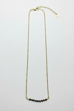 A delicate gold chain necklace with a short curved row of small black beads at the center, displayed against a plain white background.